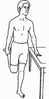 Shirtless man standing on one leg, balancing with a hand on a table. He is reaching behind with his hand on his ankle, pulling his foot up towards his buttocks.